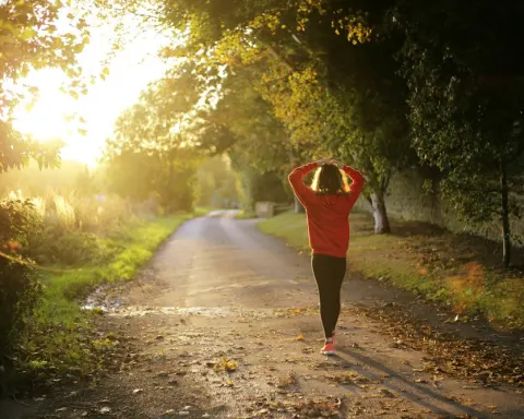 Mujer caminando por un sendero entre árboles al atardecer