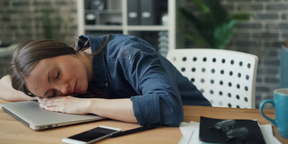 Mujer dormida sobre su escritorio junto al portátil