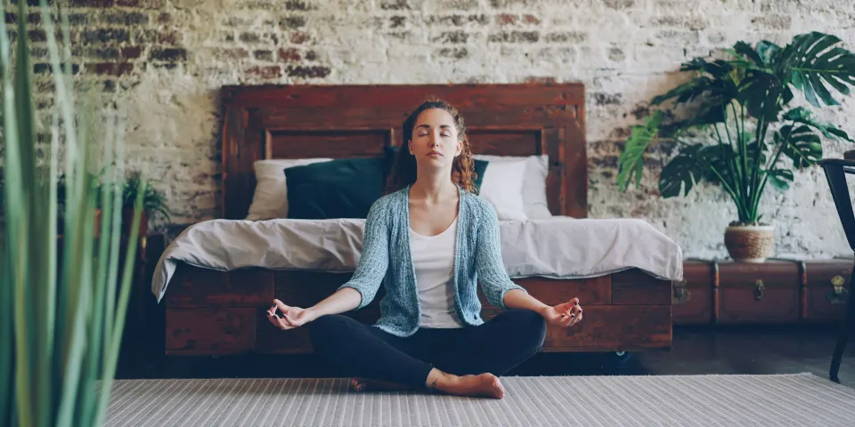 Mujer meditando con las piernas cruzadas en el piso de su habitación