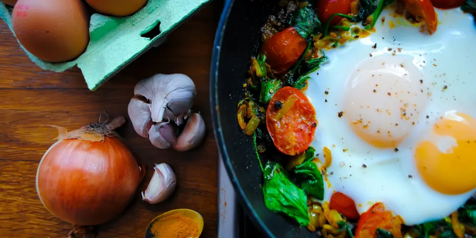 Sartén con huevos, espinaca y tomates junto a huevos frescos y cebolla