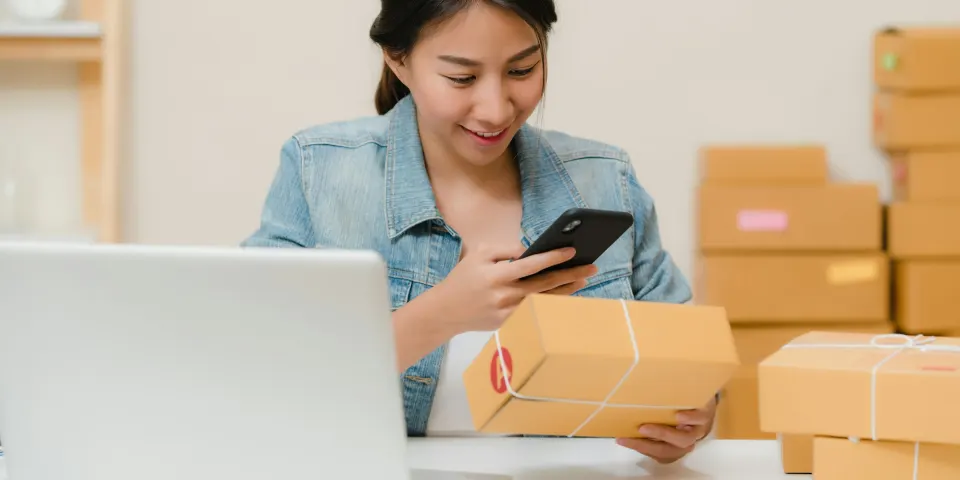 Mujer emprendedora revisando pedidos en el celular junto a cajas