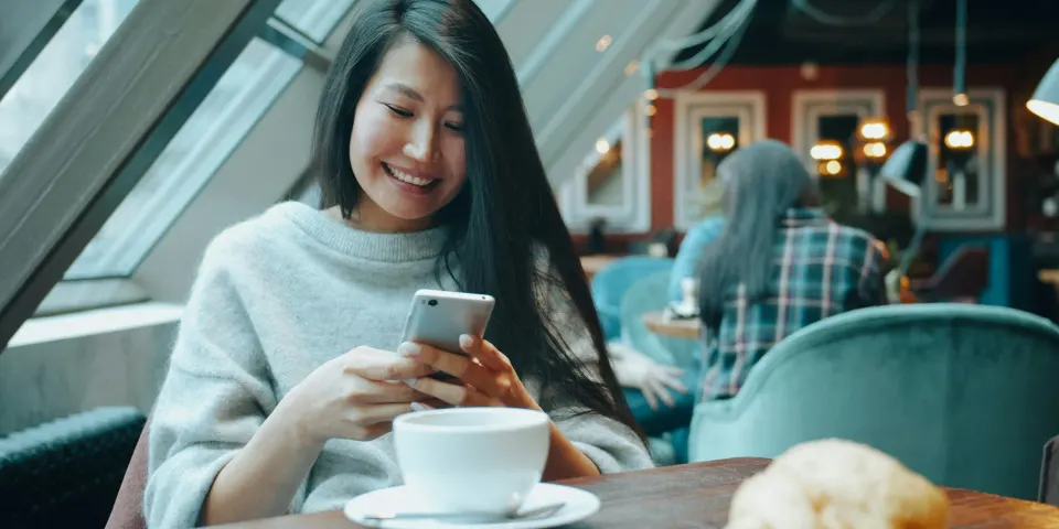 Mujer sonriendo mientras escribe en el celular con un café