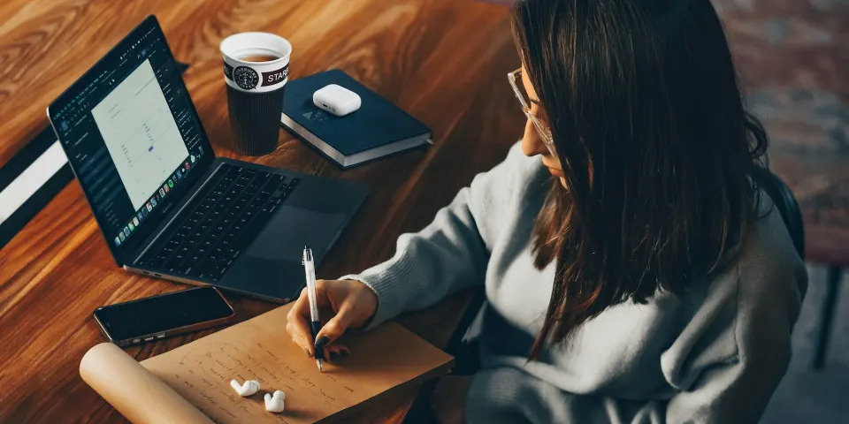 Mujer tomando notas en una libreta junto a su portátil