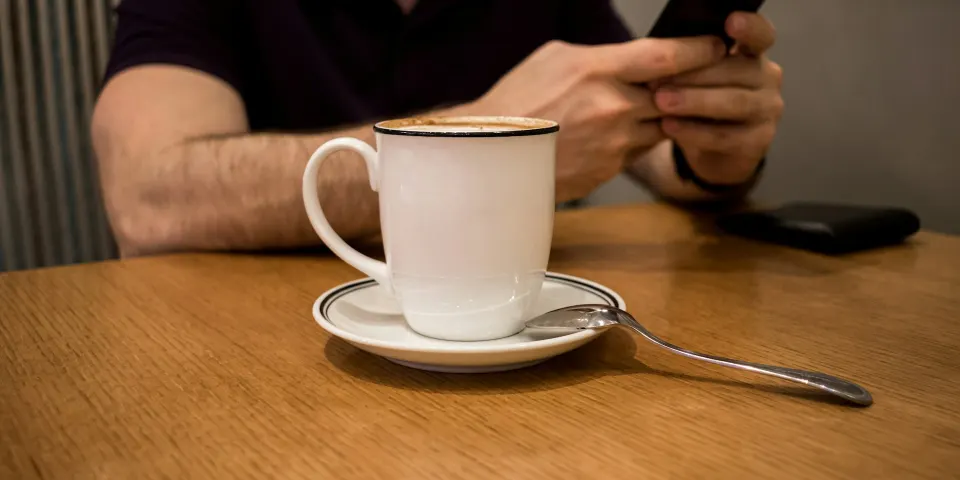 Persona usando el celular junto a una taza de café