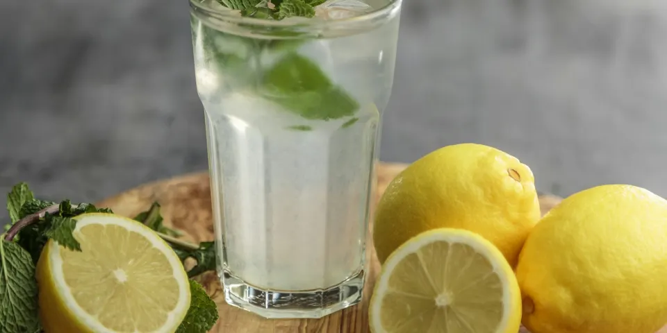 Vaso de bebida con limón y hierbabuena junto a limones