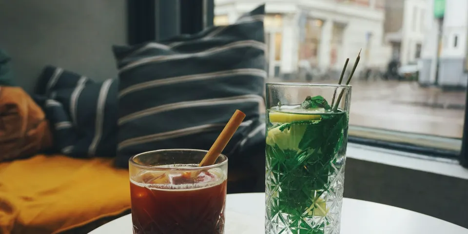 Un vaso de café frío y un vaso de té con limón y hierbabuena sobre una mesa