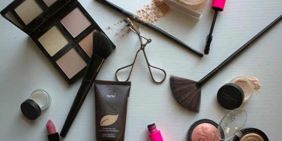 Paleta de sombras, brochas, labial, base y rubor sobre una mesa blanca