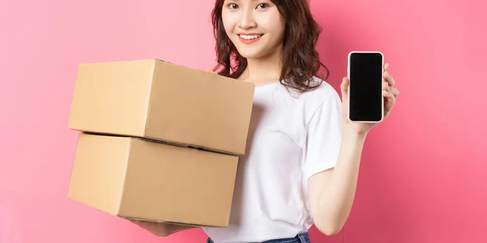 Mujer sonriente con cajas de pedidos y su celular